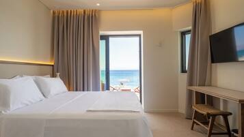 A hotel room with a bed, a desk, a chair, a TV, and a view of the sea.