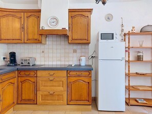A kitchen with wooden cabinets, a white refrigerator, a coffee maker, a toaster, and a clock on the wall. - Sainte Marguerite by Interhome (Saint-Tropez)