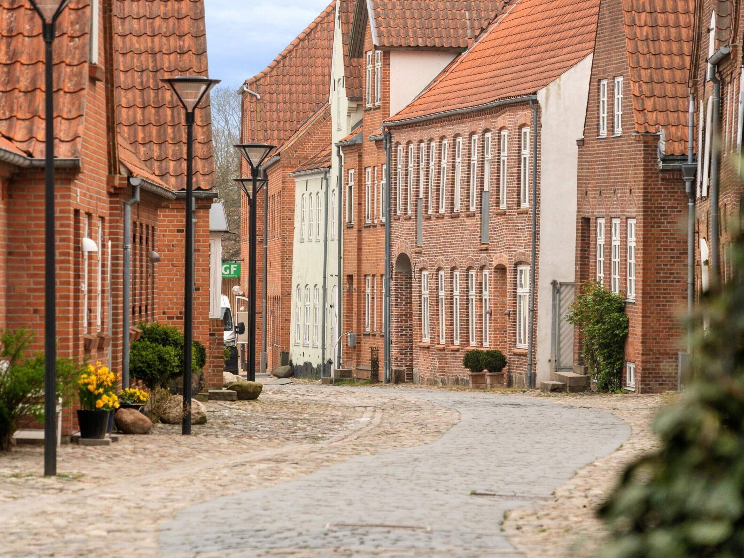 A cobblestone street lined with traditional brick buildings, a clear sky, and a green sign.