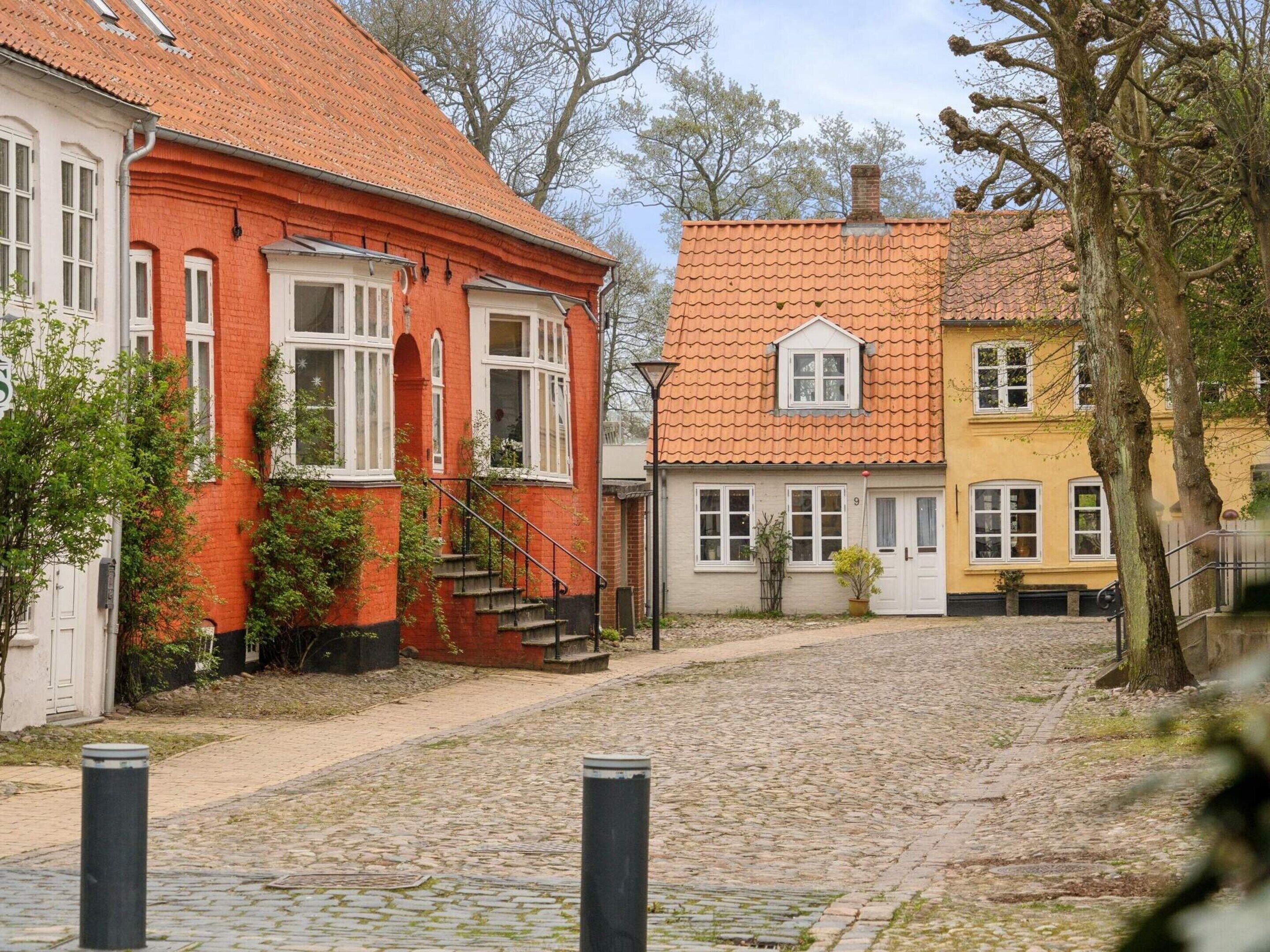 A cobblestone street with buildings featuring red and yellow facades, a staircase, and a tree.