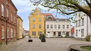 Ein Kopfsteinpflasterplatz mit historischen Gebäuden, einer zentralen Bank und einem Baum.