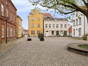Ein Kopfsteinpflasterplatz mit historischen Gebäuden, einer zentralen Bank und einem Baum.
