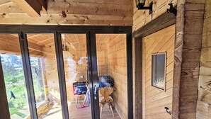 Et træhusinteriør med en skydedør af glas, der fører til en balkon, et lille bord med en stol, og en ophængt lanterne.