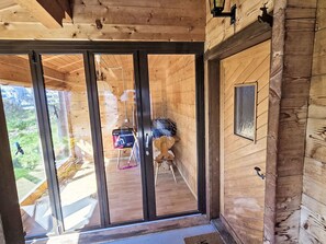 Ein Holzblock-Interieur mit einer Schiebetür aus Glas, die auf einen Balkon führt, einem kleinen Tisch mit Stuhl und einer Wandleuchte.