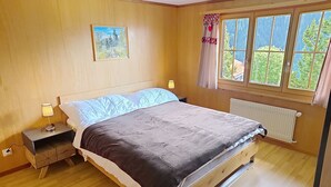Et soveværelse med en træseng, et natbord med lampe, et vindue med udsigt til grøn natur, og et maleri på væggen.