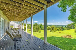 Una terrazza esterna coperta con sedie e tavolo in legno, affacciata su un paesaggio verde.