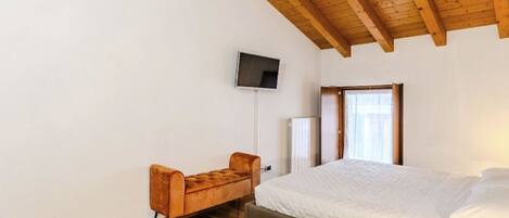 A bedroom with a wooden ceiling, a bed, a TV mounted on the wall, and a window with curtains.