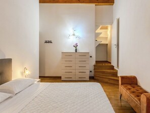 Ein Schlafzimmer mit einem Bett, einem Nachttisch, einer Kommode, einer Wandleuchte und einer Treppe, die in einen anderen Raum führt.