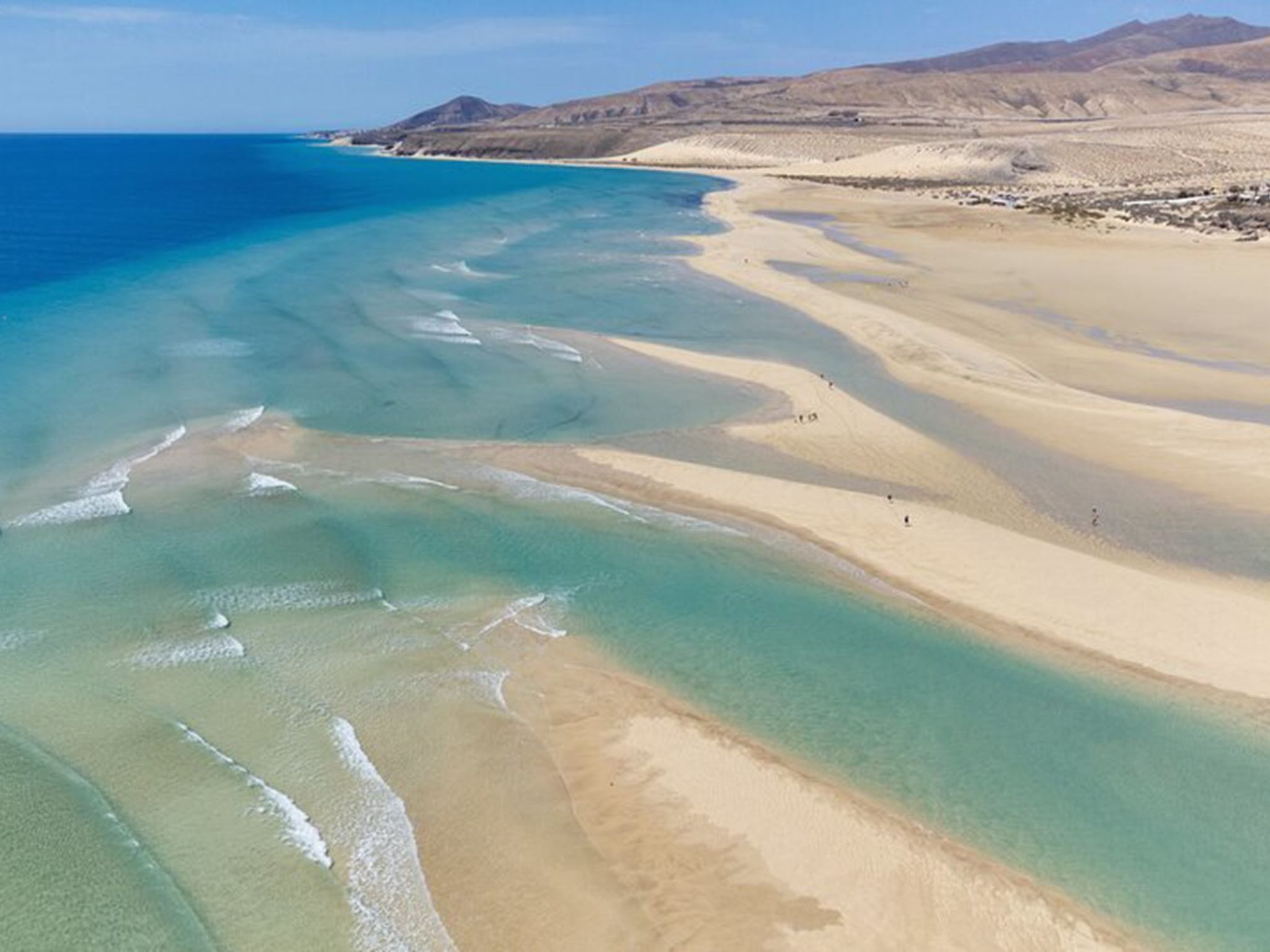 A coastal landscape with a sandy beach and clear blue waters.
