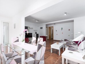 Uma sala de estar moderna com uma mesa de jantar de vidro, assentos confortáveis, uma TV de tela plana e um detalhe decorativo na parede.