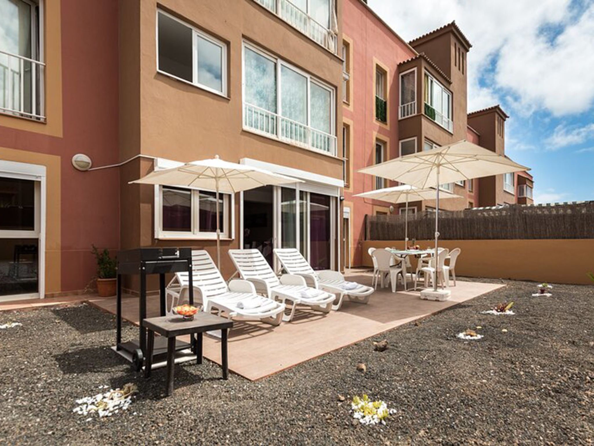 Ein Gebäude mit einer Terrasse, die Sitzgelegenheiten, Sonnenschirme und einen Grillplatz bietet.