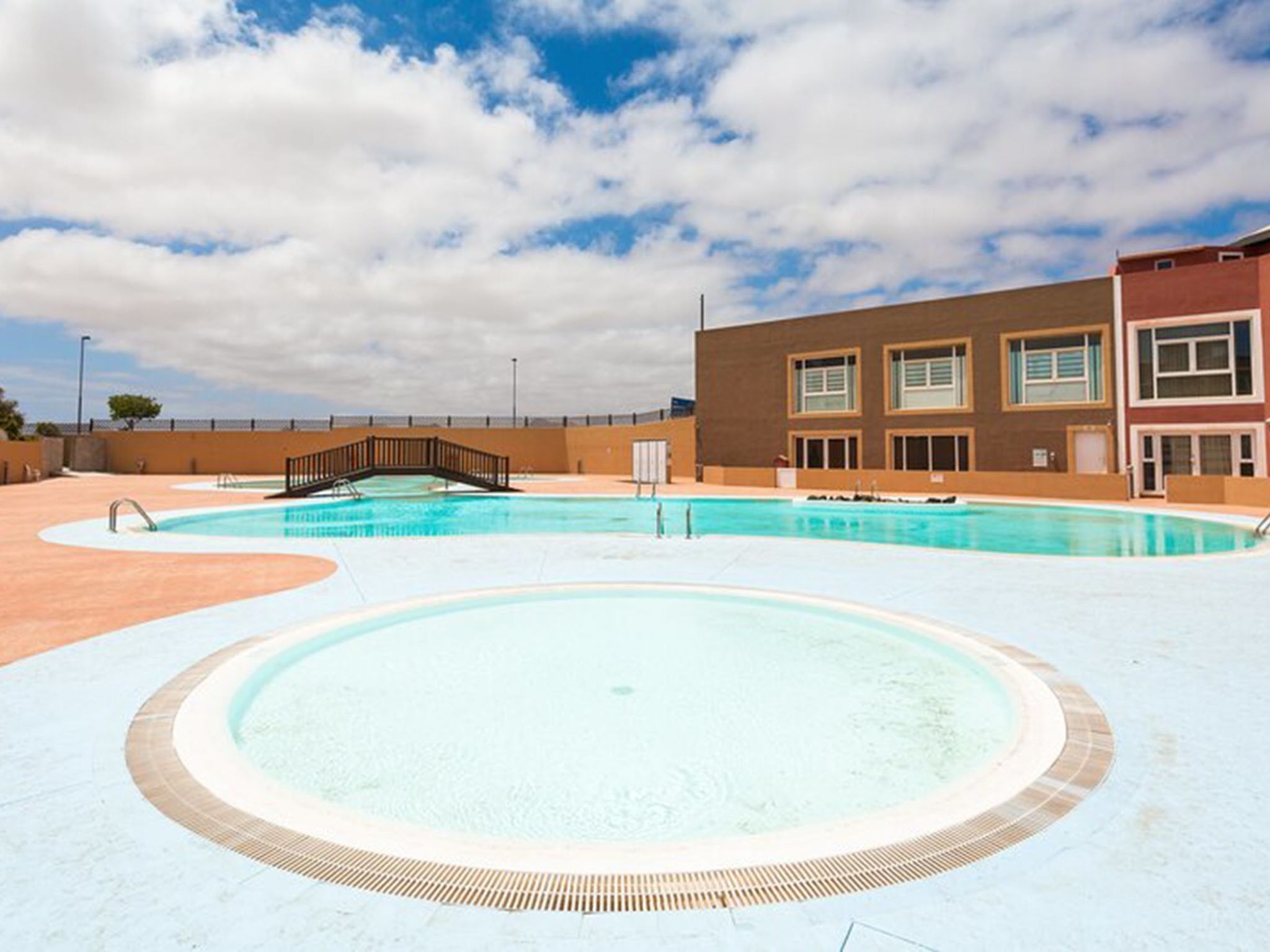 A swimming pool with a bridge, a building with multiple windows, and a clear sky.