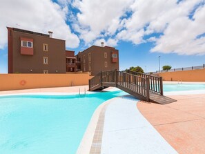 Ein Schwimmbecken mit einer Holzbrücke, angrenzenden Gebäuden und wolkenlosem Himmel.