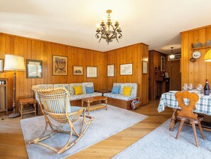 A wooden-paneled room with a sofa set, a rocking chair, a dining table with chairs, and a chandelier. - Baita del Sole by Interhome (Bormio)