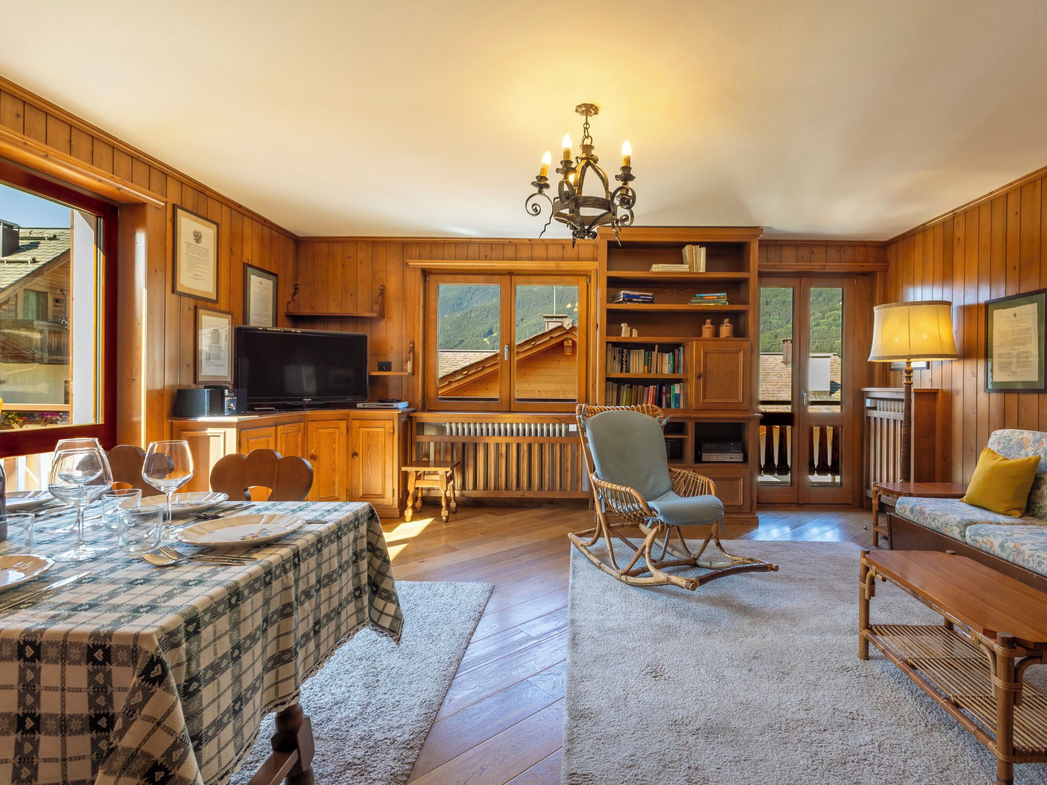 Une pièce chaleureuse avec une table à manger dressée, un téléviseur, des étagères à livres, un fauteuil à bascule et un canapé.