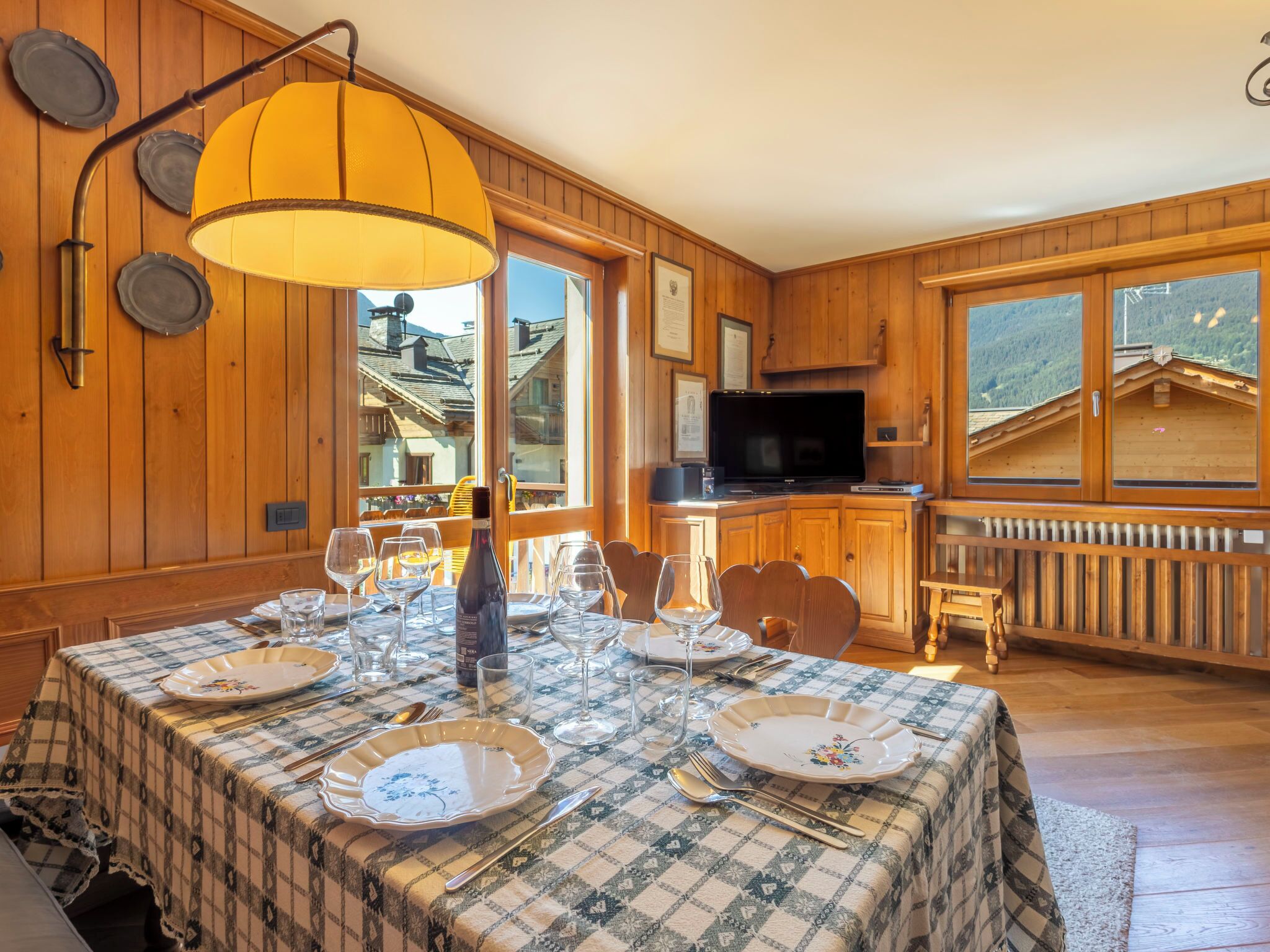 Un coin repas avec une table dressée pour quatre personnes, une bouteille de vin et un téléviseur en arrière-plan.