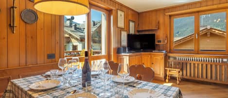 Un coin repas avec une table dressée pour quatre personnes, une bouteille de vin et un téléviseur en arrière-plan.