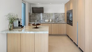Une cuisine moderne dotée d’un plan de travail en marbre, de meubles en bois, d’un four encastré et d’un téléviseur placé au-dessus de la cuisinière.