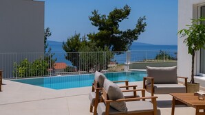 Un espace aménagé au bord de la piscine, avec vue sur la mer, comprenant des meubles d’extérieur et une rambarde.