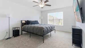 Un dormitorio con cama, ventilador de techo, mesita de noche, cómoda y ventana con persianas.