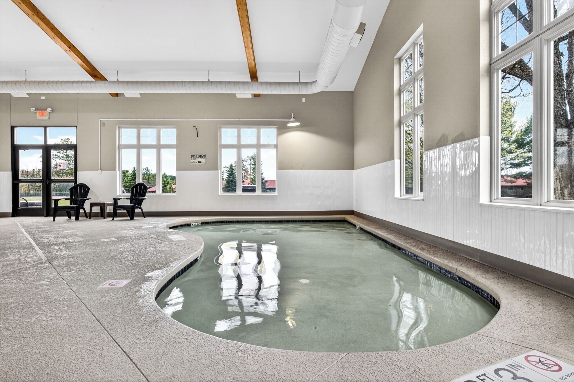 An indoor swimming pool with a curved edge, a ceiling with wooden beams, and large windows.