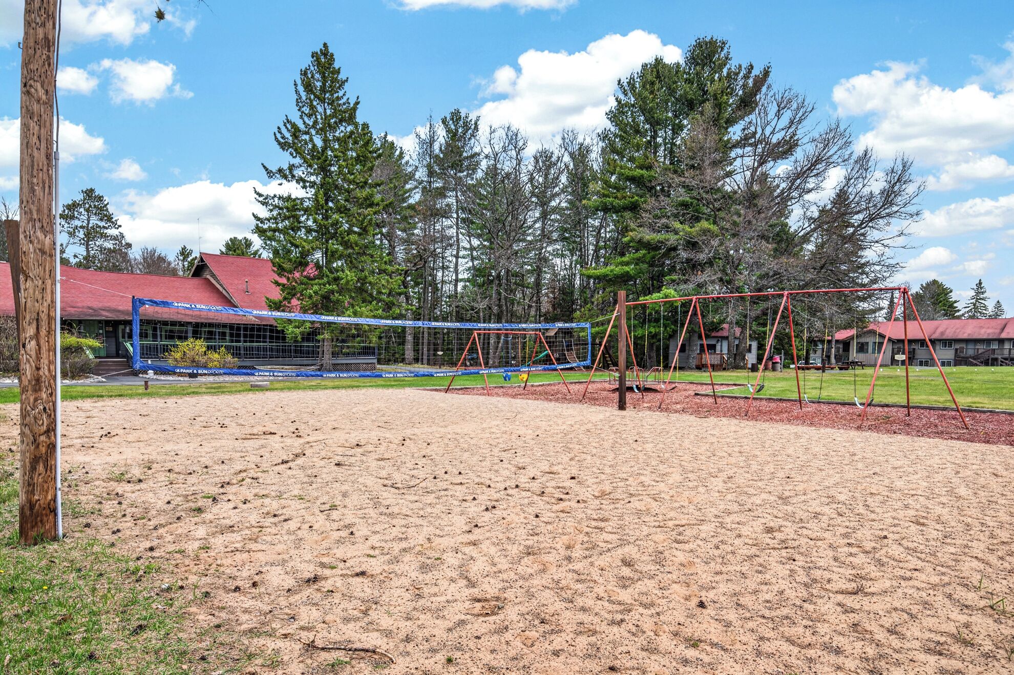 A sandy volleyball court with a net, surrounded by trees and a building with a red roof.