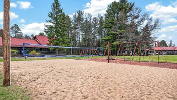 A sandy volleyball court with a net, surrounded by trees and a building with a red roof.