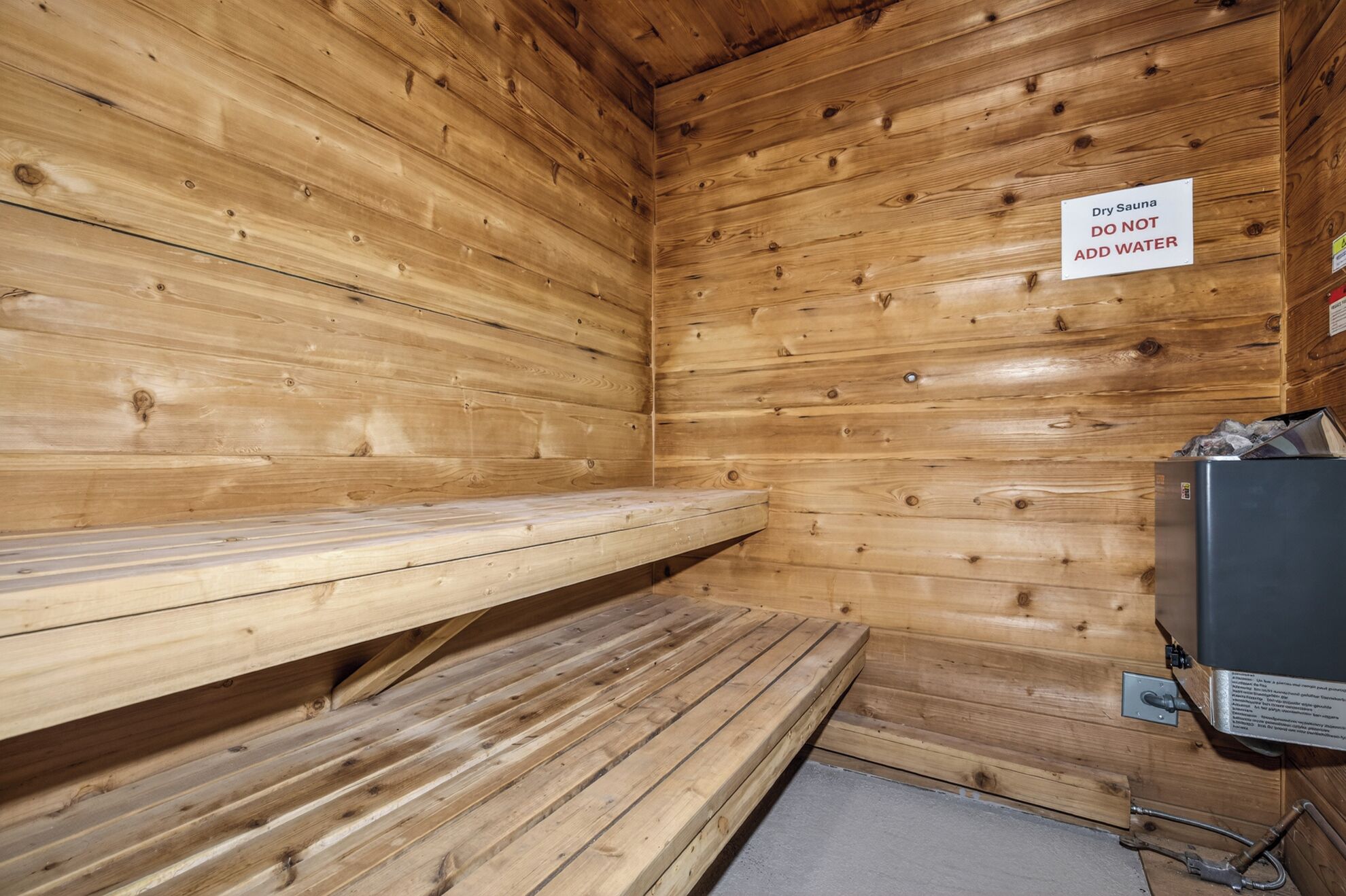 Un sauna sec avec des murs et des bancs en bois, un panneau indiquant qu’il ne faut pas y ajouter d’eau, et un téléviseur sur le côté droit.