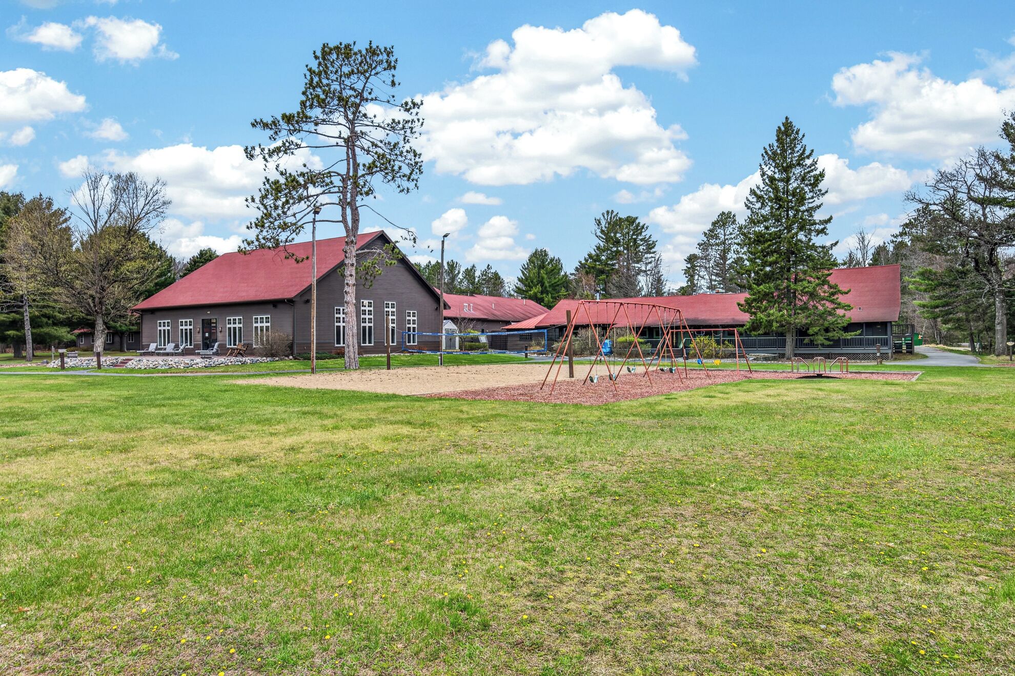 A building with a red roof, a playground with swings, and a grassy field.