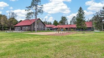 A building with a red roof, a playground with swings, and a grassy field.