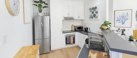 Una cocina moderna con armarios blancos, un refrigerador de acero inoxidable, una encimera de madera y un horno integrado.