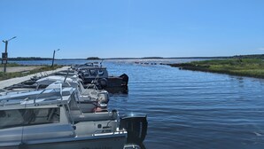 Un puerto deportivo con barcos amarrados a lo largo de una vía fluvial tranquila, cielo despejado y una costa lejana.