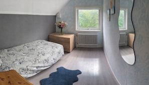 A bedroom with a bed, dresser, radiator, window, and mirror.