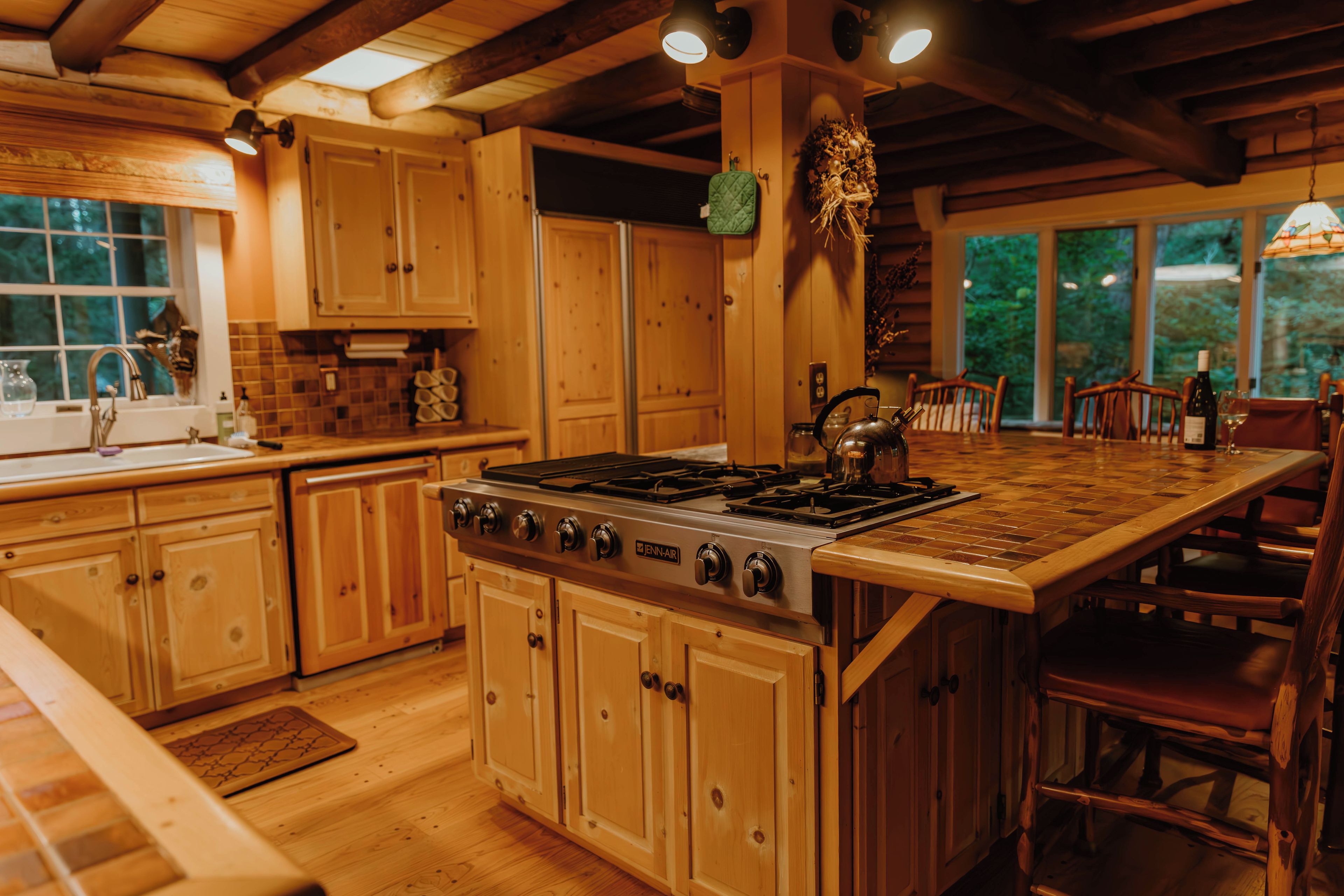 A kitchen with wooden cabinets, a large island with a stove, and a dining area with chairs.