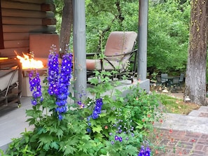 A patio area with a fire feature, a chair, and surrounding greenery.