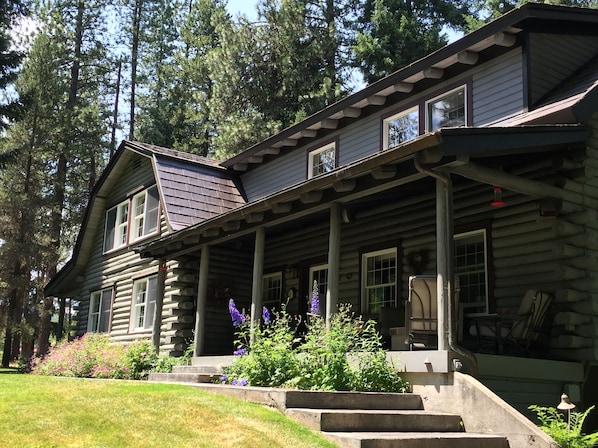 A log cabin with a porch, steps, and a garden with flowers.