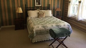 Um quarto com cama, mesa de cabeceira, luminária, janela com cortinas e edredom acolchoado.