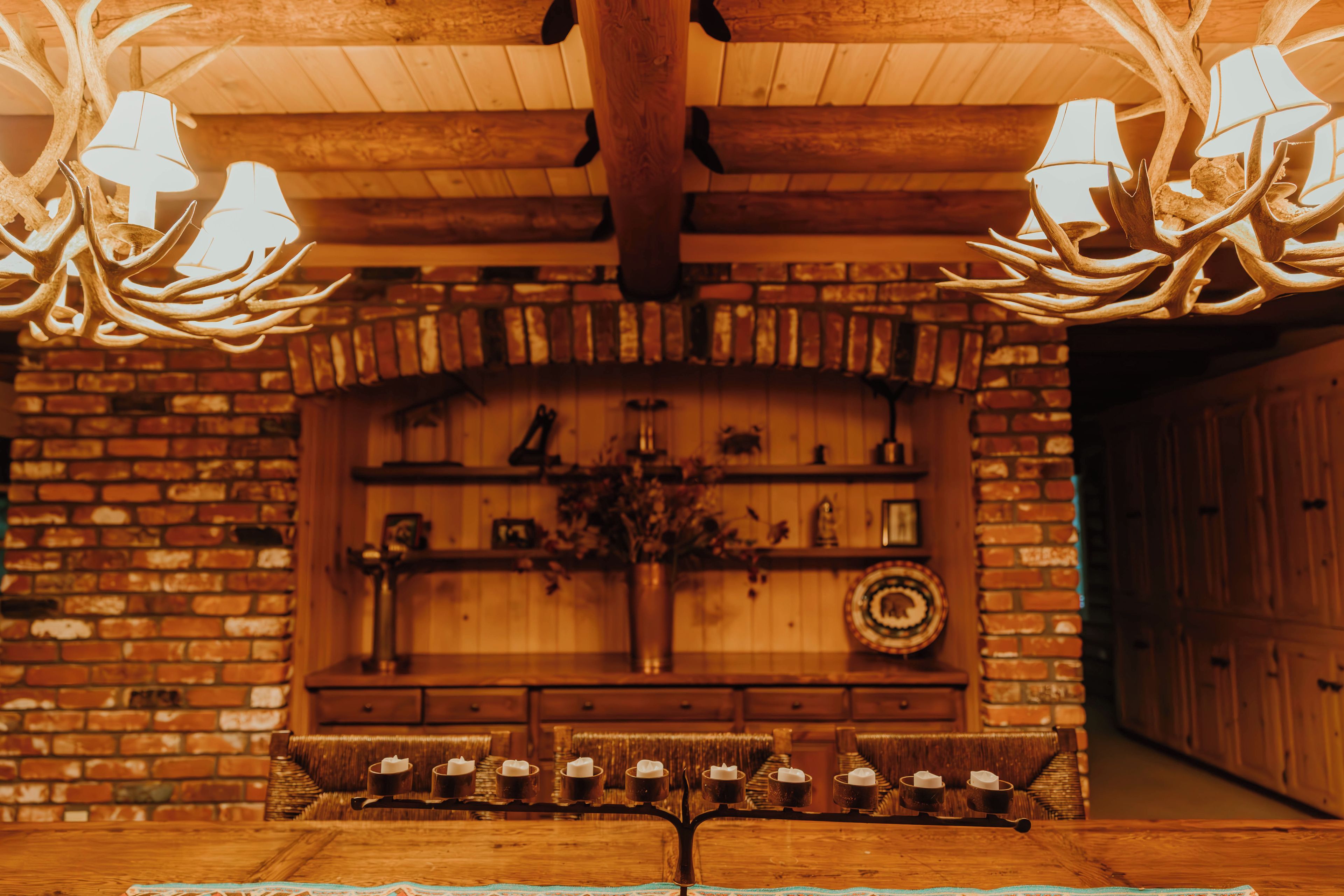 A cozy interior with a brick fireplace, wooden ceiling, and a table with candles.