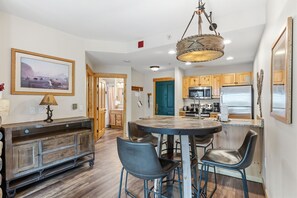 A modern kitchen with wooden cabinets, a central island, and a dining area with chairs. - Copper Mountain Center Village Condo | Halfpipe Views, Walk to Lifts (Frisco)