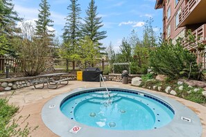 A hot tub surrounded by a stone wall, trees, and a wooden fence. - Copper Mountain Center Village Condo | Halfpipe Views, Walk to Lifts (Frisco)