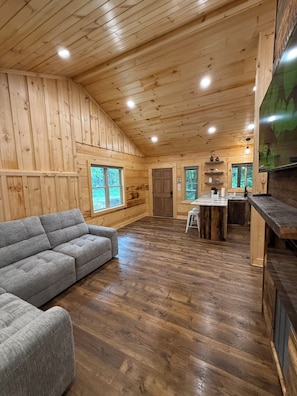 Ein Holzblock-Interieur mit einer Couch, einer Küchenzeile und großen Fenstern.