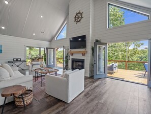 Ein geräumiges Wohnzimmer mit Kamin, Fernseher und großem Fenster mit Blick auf eine Terrasse.