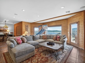 A spacious living room with a large sectional sofa, a coffee table, and a view of a lake through large windows.
