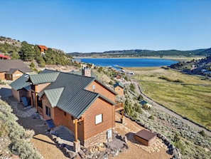 A wooden cabin with a sloped roof, a stone foundation, and a view of a lake and hills.