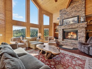 A spacious living room with a stone fireplace, large windows, and a cozy seating area.