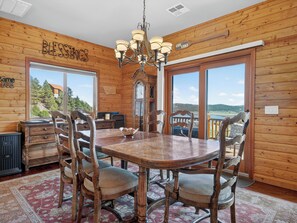 A wooden interior with a dining table, chairs, a chandelier, and a view of a lake.