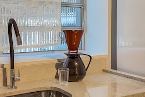 A kitchen with a sink, a coffee maker, and a window with a view of buildings. - Aconchego Cotoxó (São Paulo)