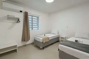 Quarto pequeno e limpo com uma cama, mesa de cabeceira, janela com cortinas e ar condicionado fixado na parede.