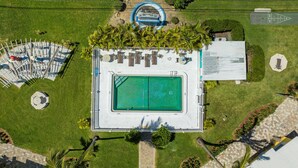 Vista aérea de un área de piscina con terraza, sillas de descanso y palmeras.