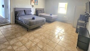 Un dormitorio con cama, un sofá pequeño, ventilador de techo y un mueble para televisión.